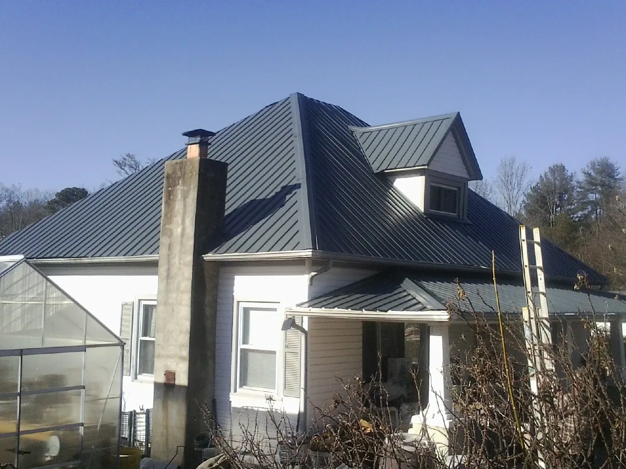 Dark blue standing seam metal roof on a white farmhouse with dormer — Slate & Tile Roof Repair by Roofing Brothers in Jeffersonville