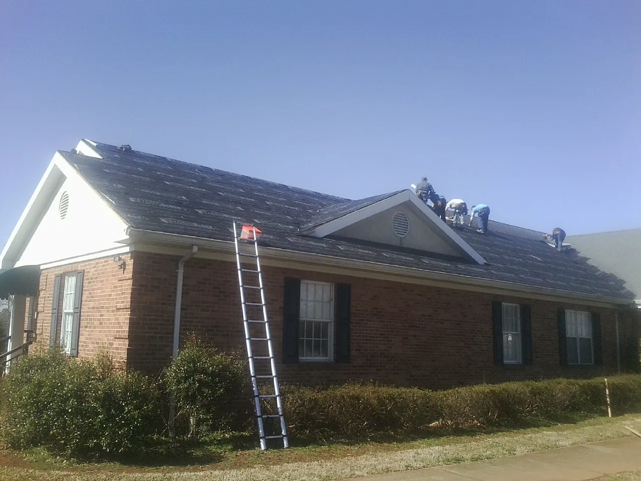 Crew tearing shingles off a brick ranch roof with a ladder set — Emergency Roof Repair work by our crew in Jeffersonville